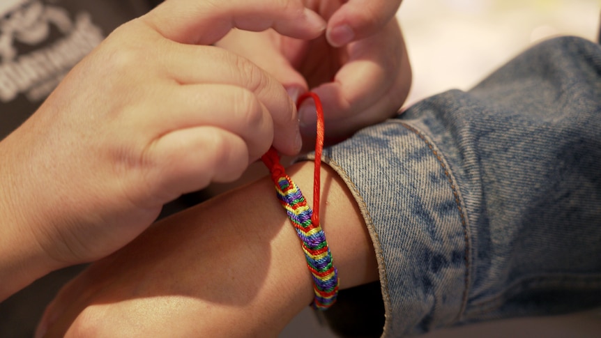 Las manos de una mujer están atando un brazalete en la muñeca de otra mujer.