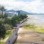 An aerial image of the promenade along the Cairns esplanade with tall buildings, mud flats and the sea on either side.