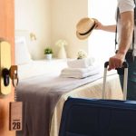 A person holding a hat and a briefcase entering a hotel room.