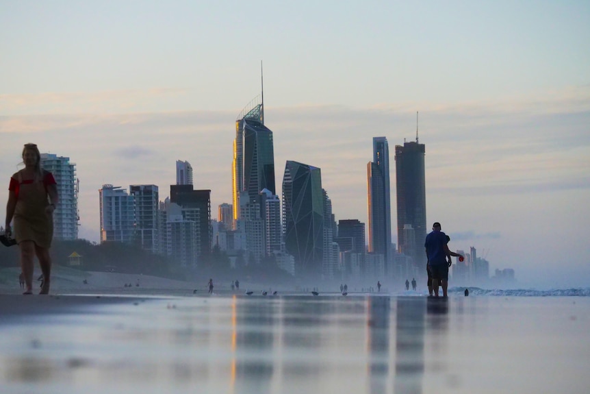 El horizonte de la ciudad detrás de la playa, dos personas caminan en primer plano, muchas de ellas en la playa detrás.