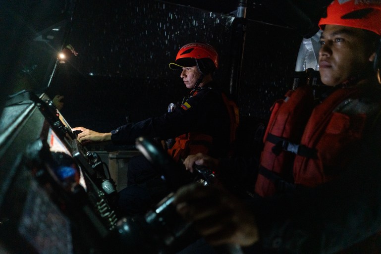 Los miembros de la Guardia Costera, vestidos con cascos naranjas y chalecos salvavidas, permanecen detrás de los controles de su barco durante una patrulla nocturna.