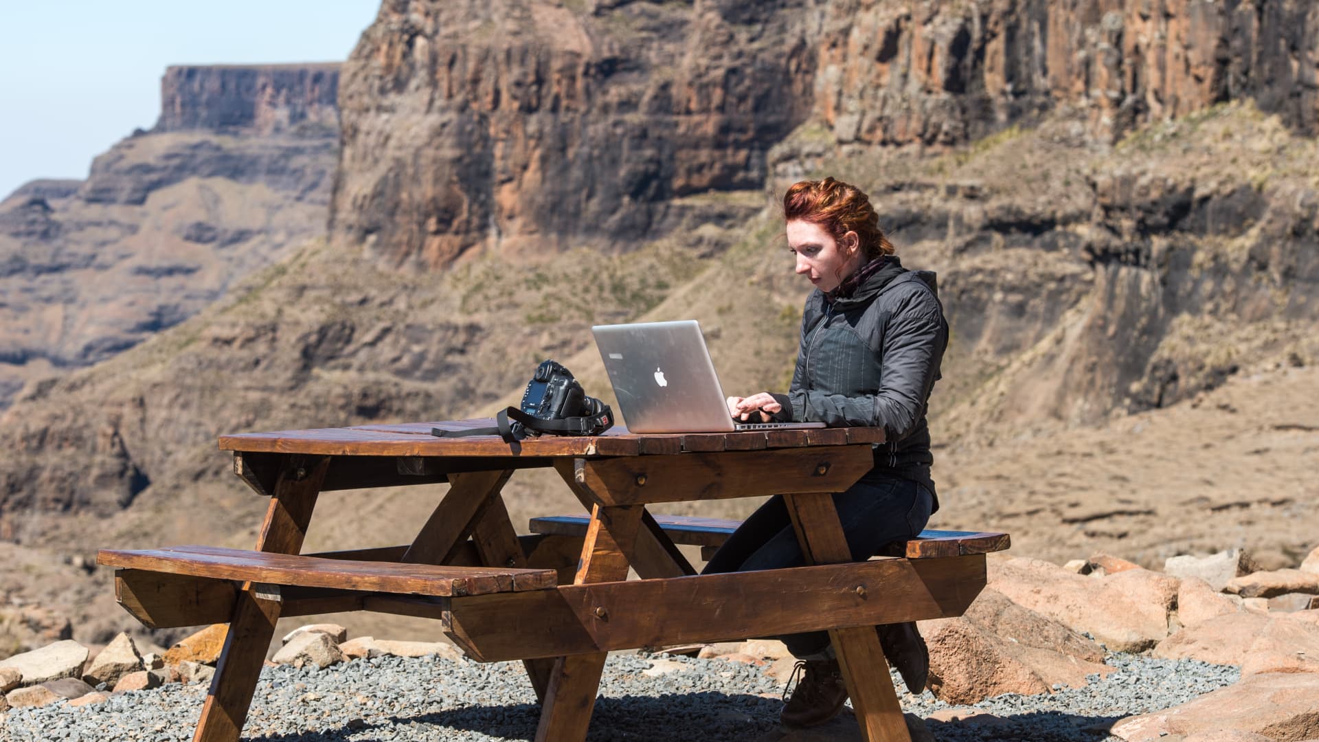 Mujer joven trabajando en su computadora portátil en una mesa de picnic en las montañas de Lesotho, África.