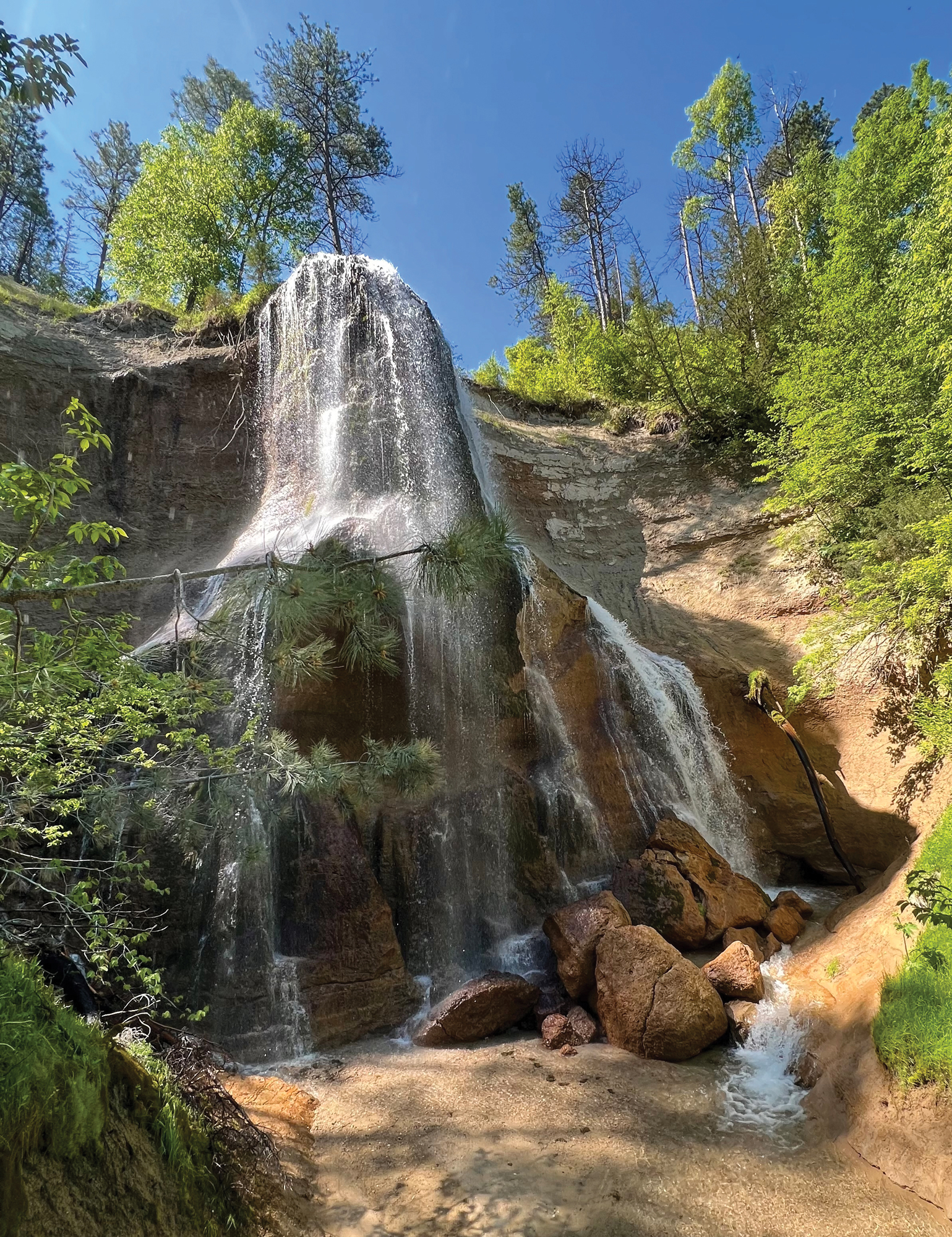Imagen de un acantilado y una cascada en Nebraska con un cielo azul sin nubes y árboles llenos alrededor de la cascada.