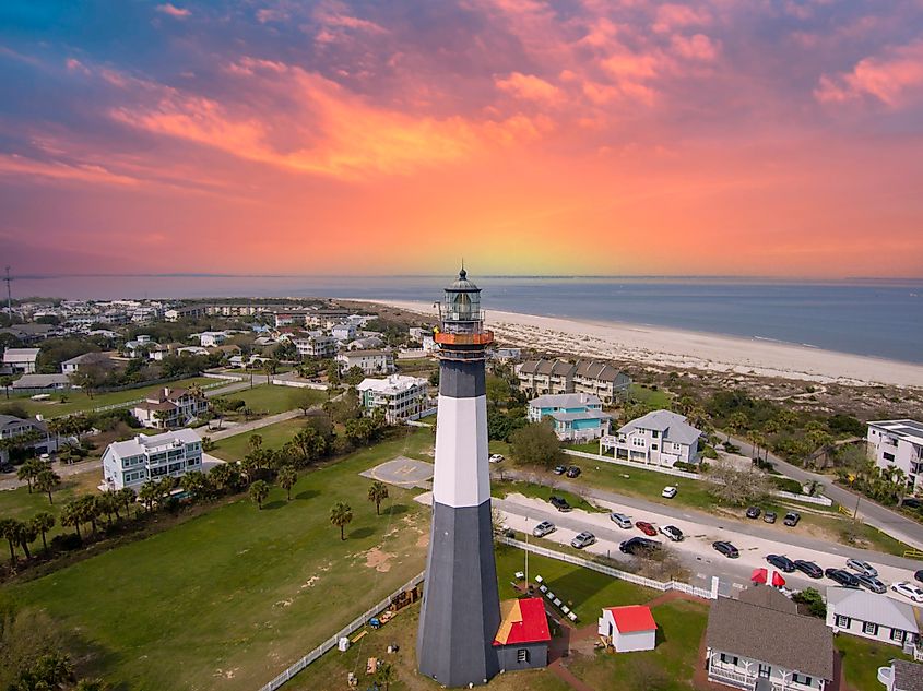 Tybee Island, Georgia: Toma aérea de un hermoso paisaje primaveral con un faro, agua azul del océano, una playa de arena, casas y frondosos árboles y césped en medio de Tybee Island.