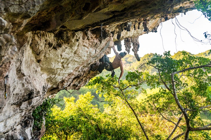Hombre escalando una cueva de piedra caliza en Jamaica.