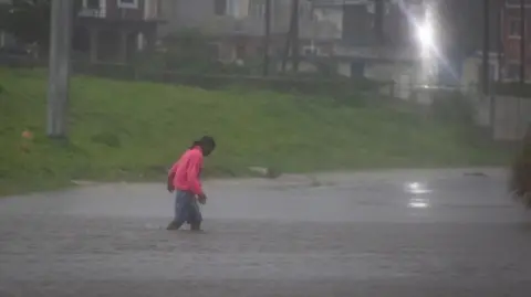 Reuters Un hombre con un jersey rosa brillante y pantalones cortos camina por una calle inundada.