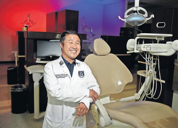 Un dentista masculino que usa una bata de laboratorio se encuentra con una silla de higiene dental.