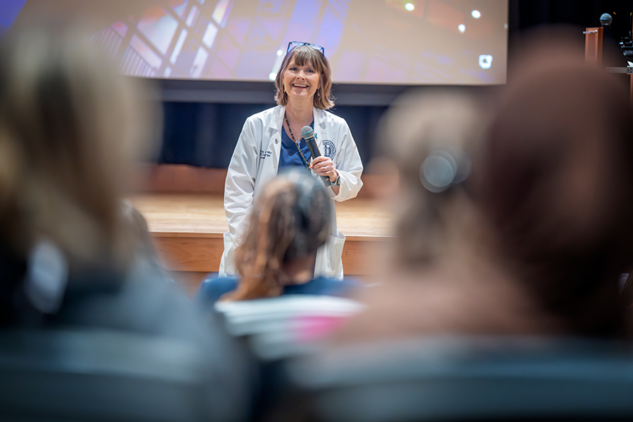 Una profesora de universidad, con matorrales médicos y abrigos de laboratorio, se encuentra frente al auditorio y se dirige a un grupo de estudiantes universitarios.
