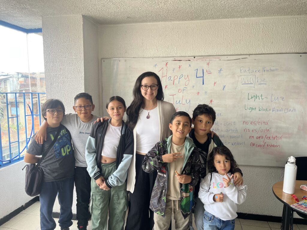 Un maestro se encuentra con seis estudiantes frente a la junta blanca decorada para el 4 de julio en un salón de clases.