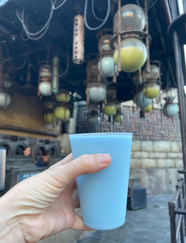 Una mano que sostiene una taza azul en el lugar inclinado con la linterna colgando la linterna colgando en el fondo