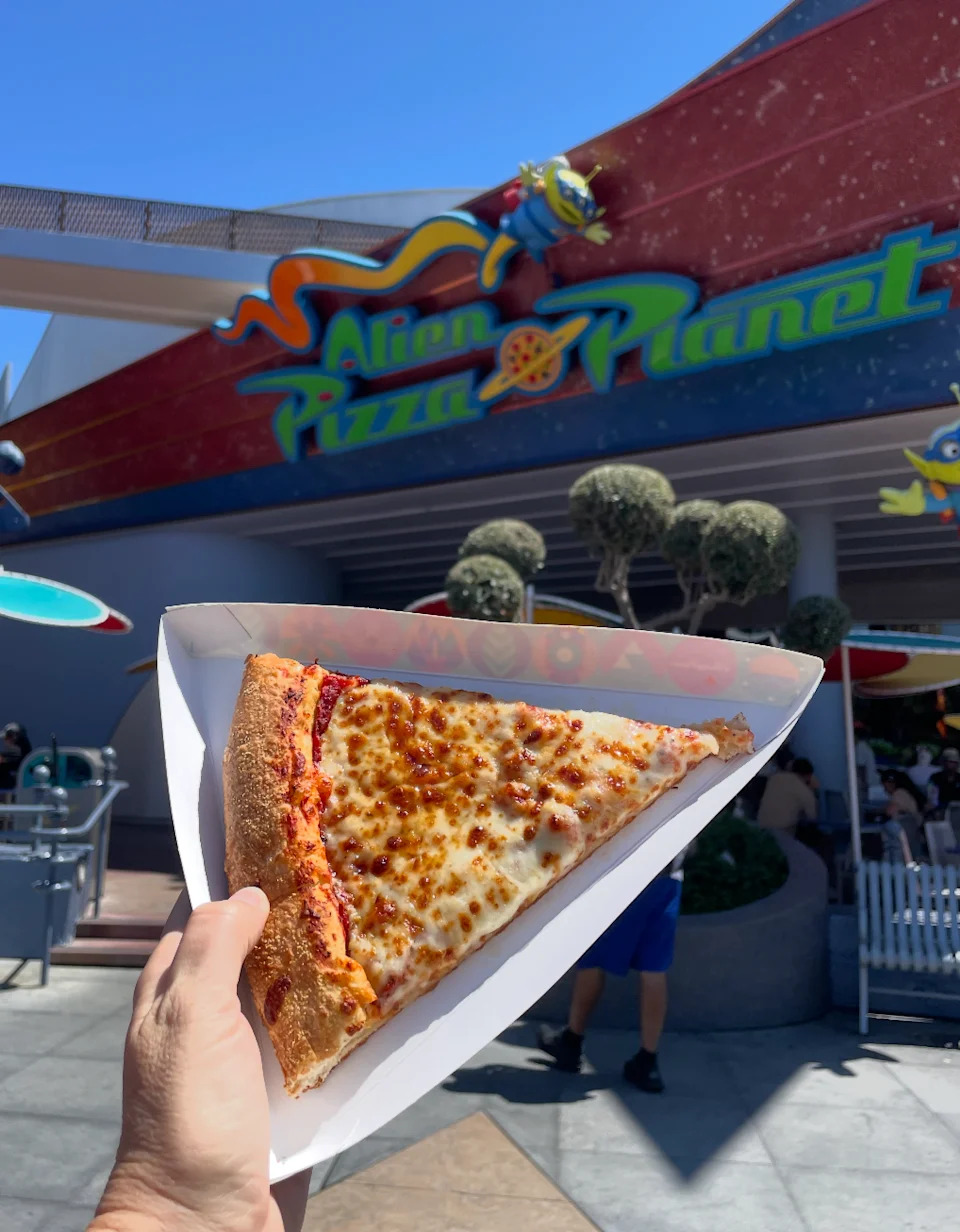 Por un lado, la pizza alienígena en el fondo es un pedazo de pizza de queso a lo largo del restaurante Planet, que incluye indicadores coloridos y una personalidad alienígena juguetona.