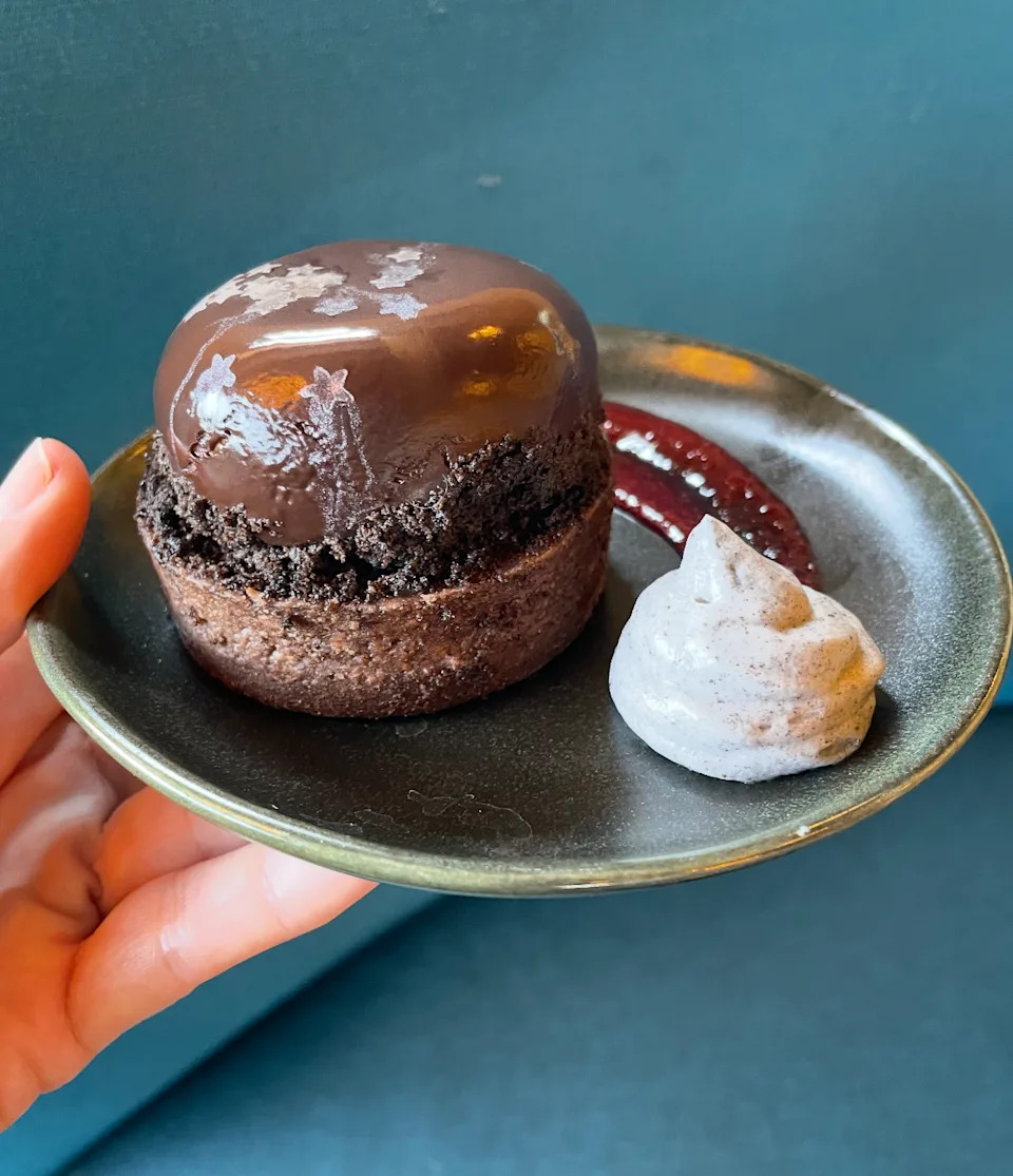 En un plato se presenta con tapa brillante con postre de chocolate gourmet, una muñeca de crema de basura y una rotación de salsa