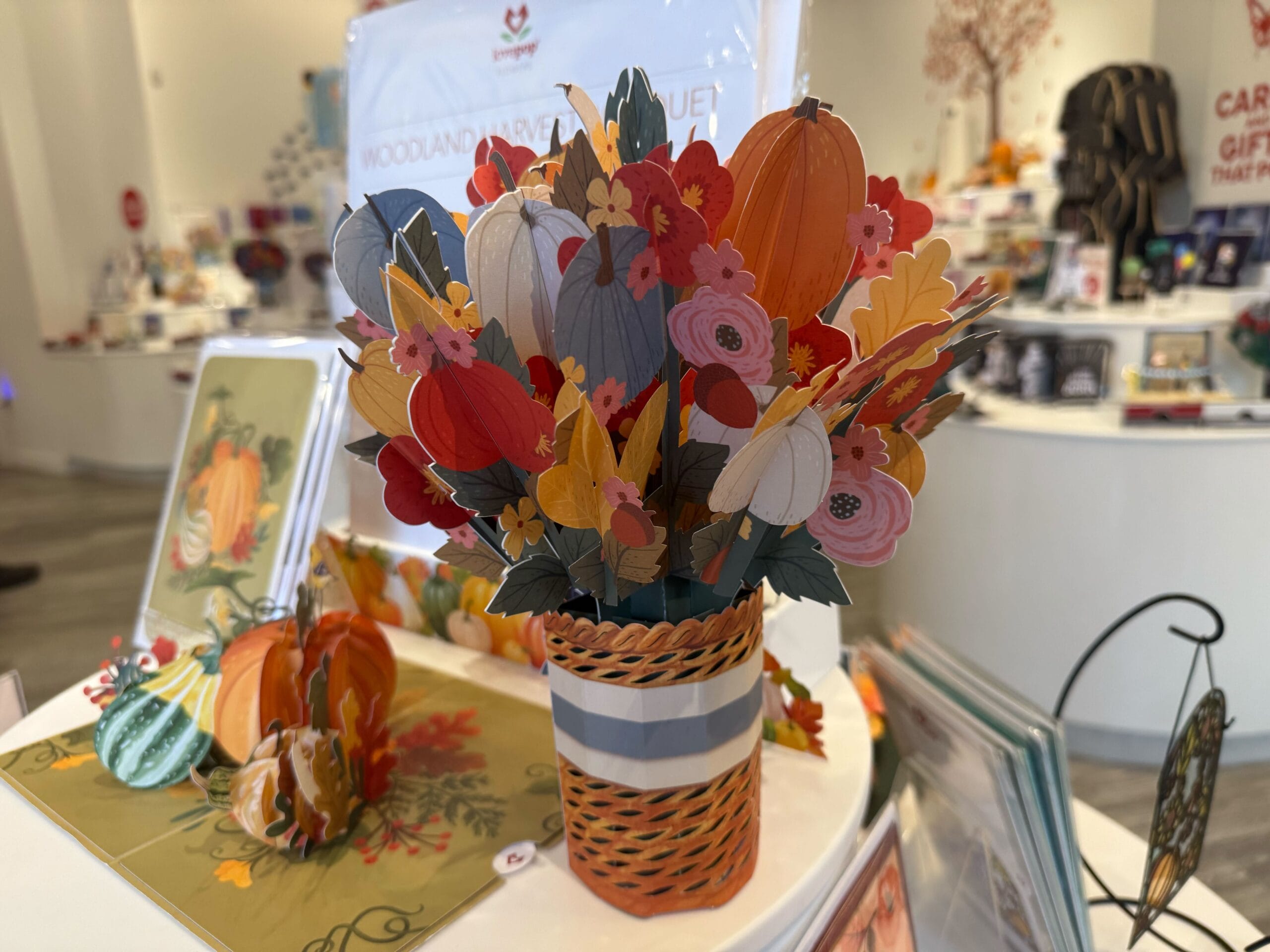 Un ramo de un papel colorido en un jarrón rayado, una calabaza y una flor, que aparece en el mostrador de la tienda.
