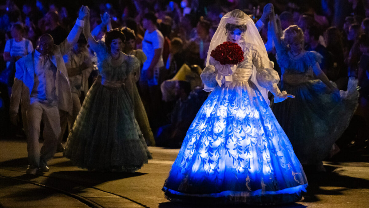 En un brillante vestido de novia azul, una mujer, la no emisión de Mickey, toca una flor roja en la fiesta de Halloween, que estaba rodeada de invitados por la noche.