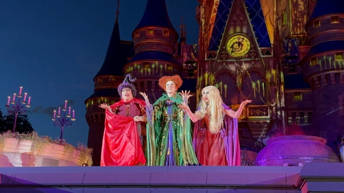 En los coloridos disfraces de brujas, tres personas actúan frente a un palacio en el escenario de la fiesta de Halloween, no Mickey.