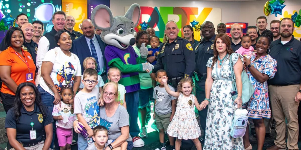 Un gran grupo de adultos y niños, incluidos oficiales de policía y un espectáculo en la camisa verde, junto con un ratón Shoebnker, una sonrisa y una brillante fiesta de decoración juntos.