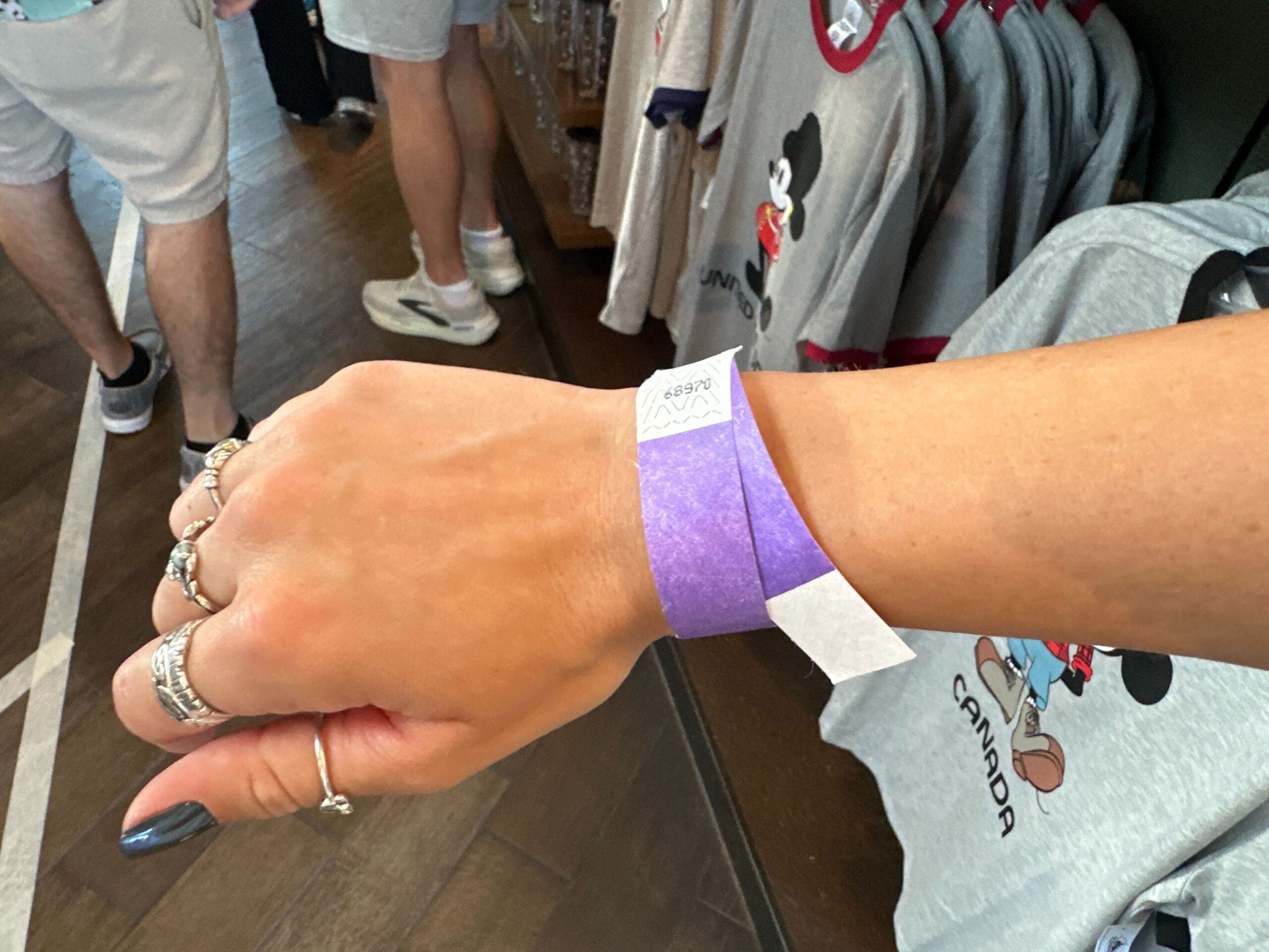 Una mano en la que los círculos plateados y una muñeca morada tienen una tienda que comercia cerca de las camisas de Mickey Mouse Canada.
