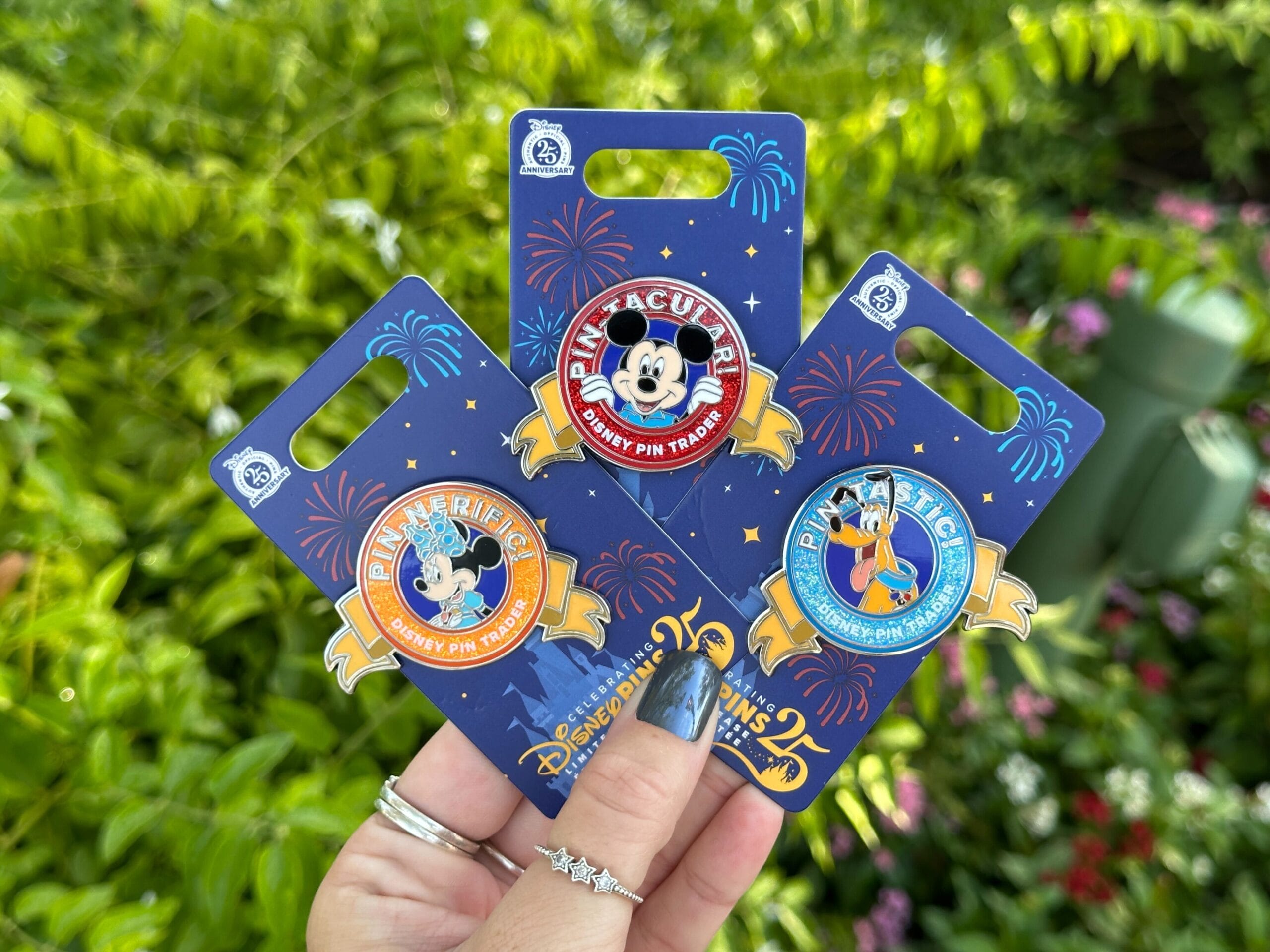El mundo de Disney, en una mano, consta del 25 aniversario de los alfileres, que presenta a Mickey y Morha, que tiene fondo verde y externo de flores.