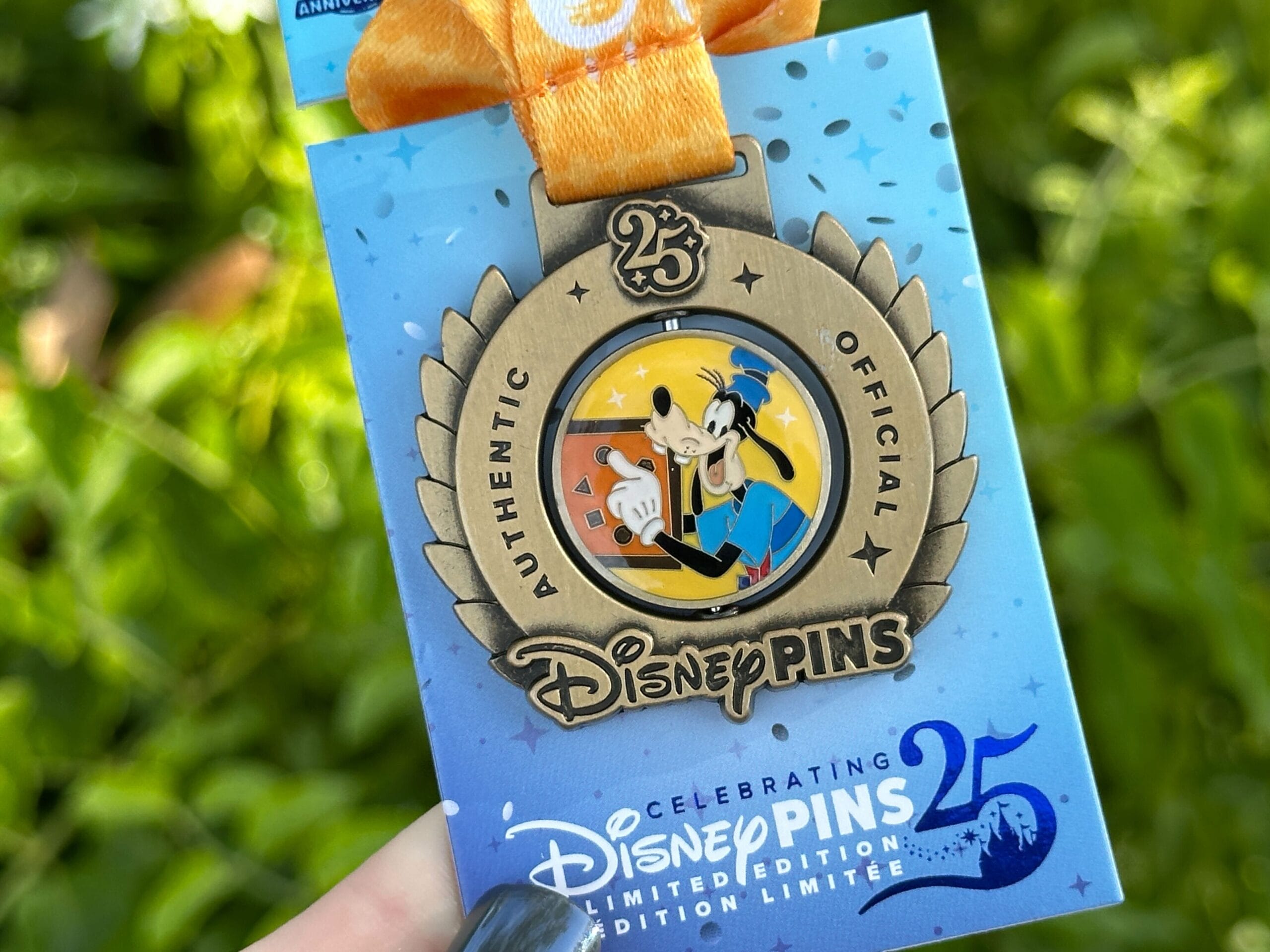 La medalla de cumpleaños número 25 de Disney Pensons, que es mejor para el comercio de pines de Disney World, está en contra del fondo borroso verde.