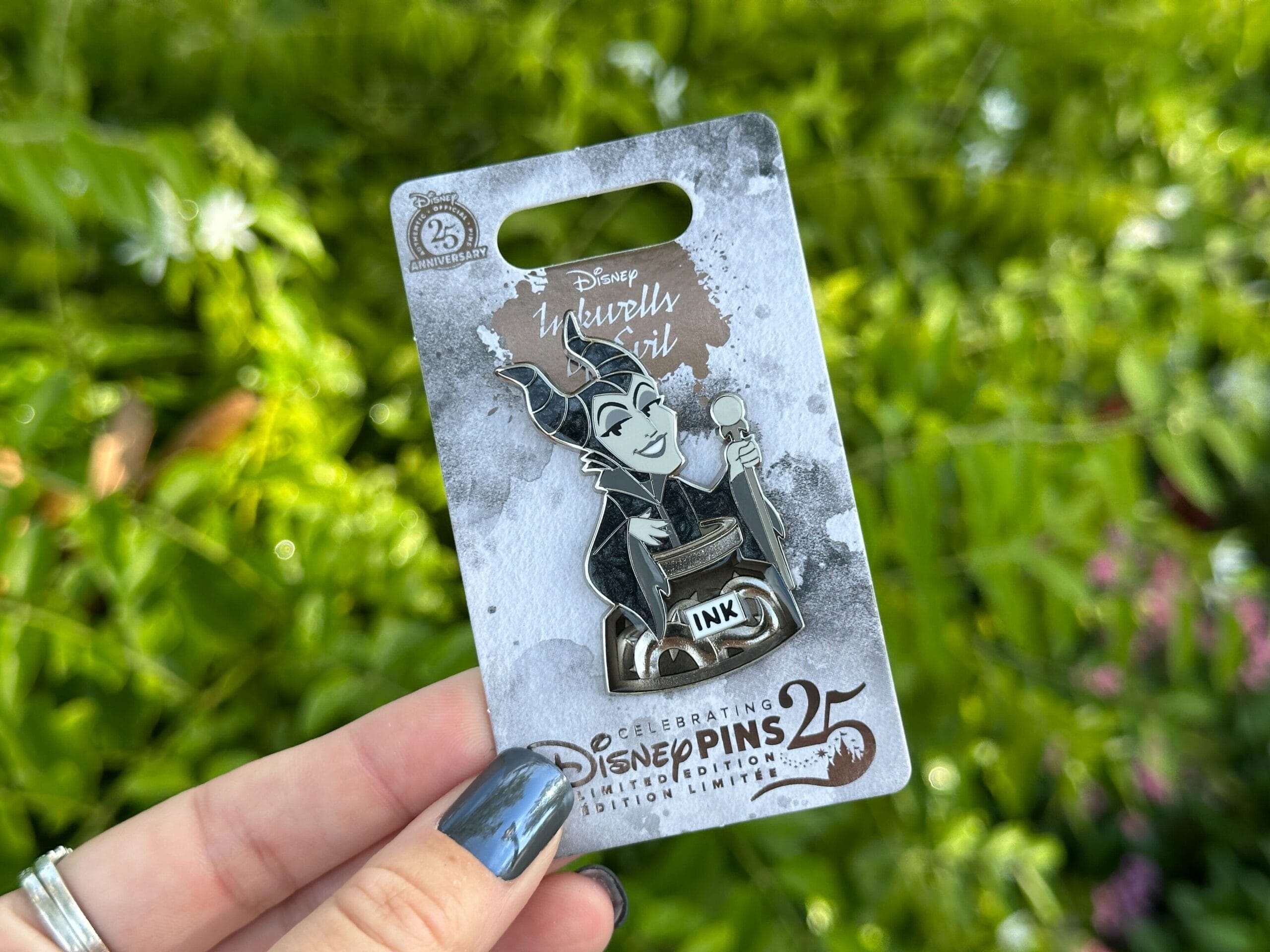 One Hand es el Pin de Melphstent de Disney World, que es excelente en el comercio de pines con vegetación en el fondo.
