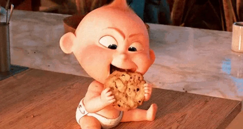 Un bebé dinámico en un pañal está comiendo una gran galleta en el mostrador de la cocina.