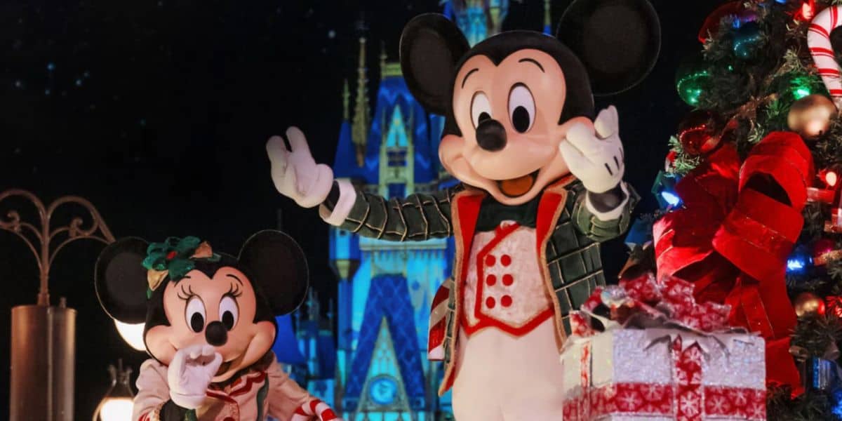 Mikey y Mini Mouse se vistieron con festivos de ropa de vacaciones cerca del árbol de Navidad decorado con regalos envueltos, disfrutando de un desfile mágico frente a un palacio brillante por la noche.