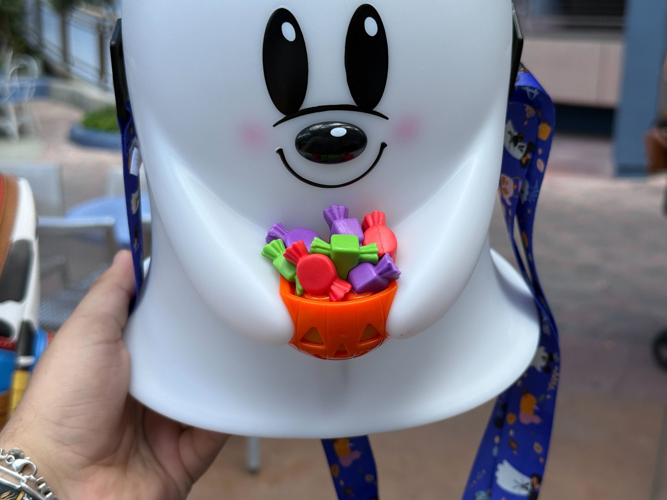 Sonriendo en una mano, el cubo de palomitas de maíz Mickey Ghost es 2025 con un pequeño cuenco de naranja de coloridos dulces de Halloween.