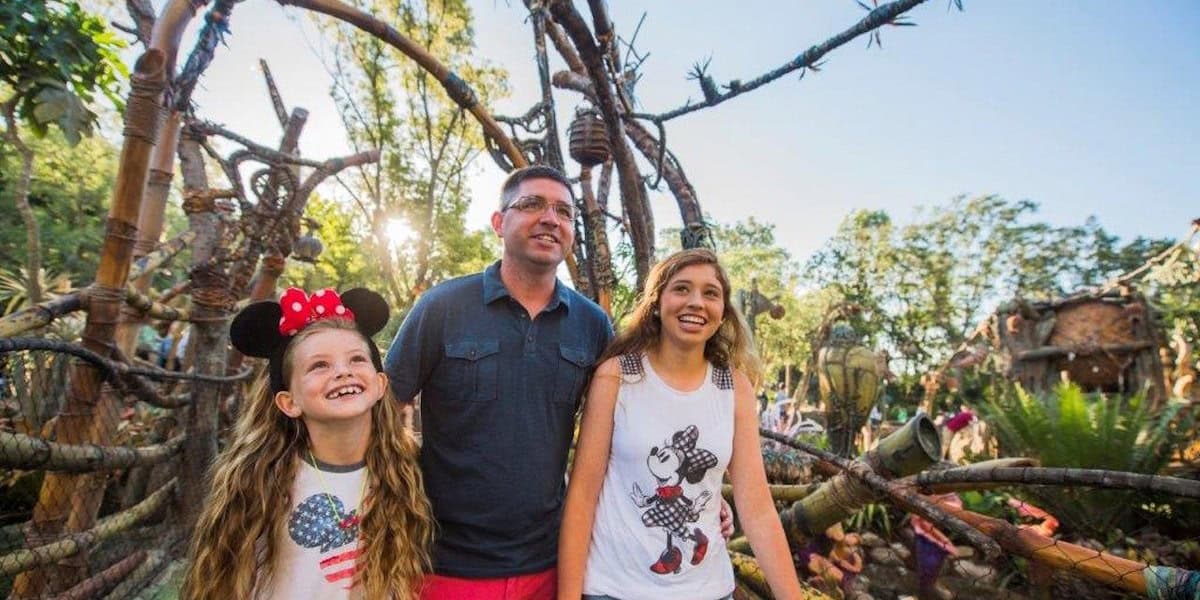Un hombre sonriente y dos chicas, con una mini oreja de ratón, de pie en Pandora, el mundo de Avatar, disfrutando de un día brillante y soleado.