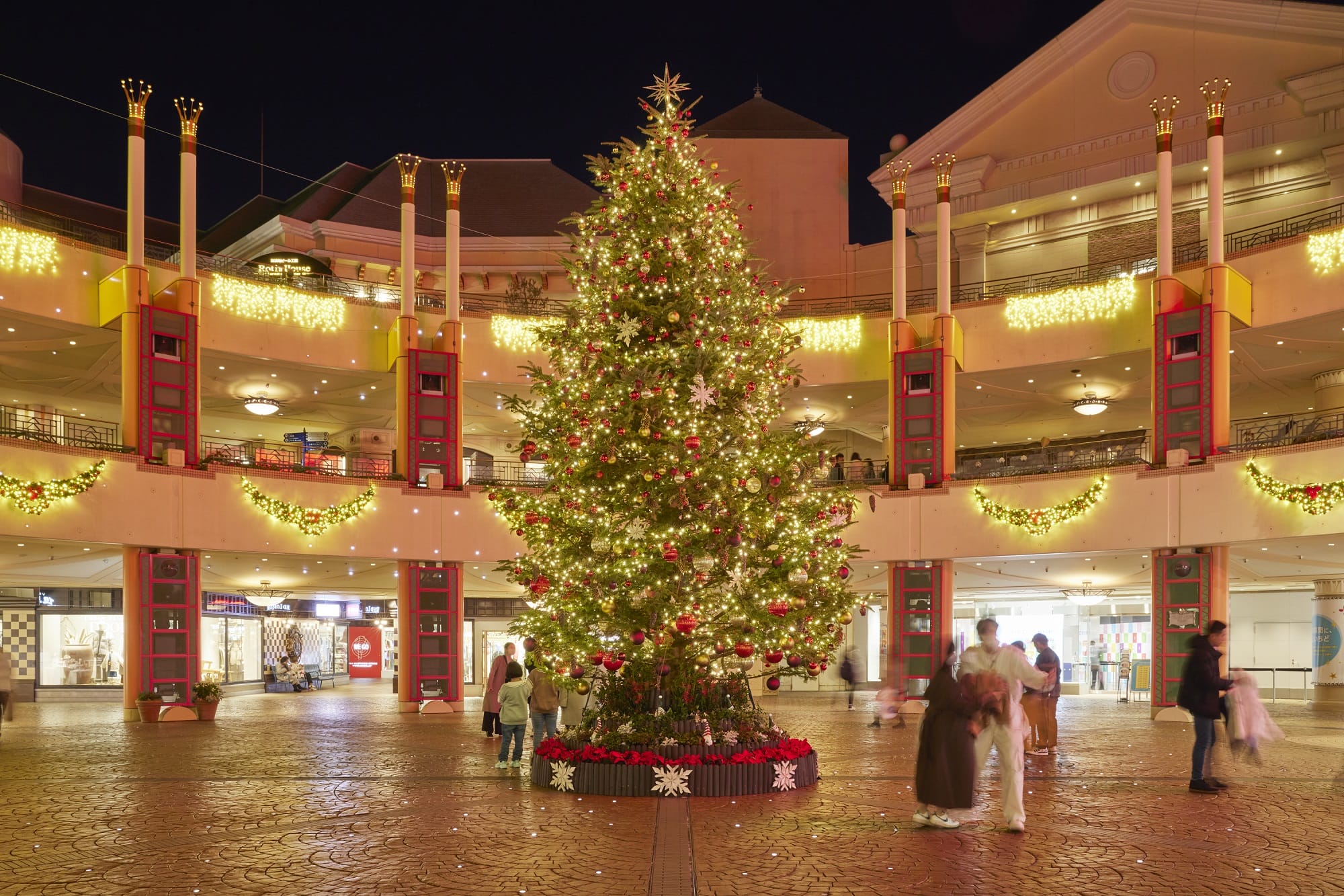 Por la noche, un árbol de Navidad brillante en una brillante plaza brillante, porque los visitantes disfrutan de un ambiente de festival de Tokio Disneyland.
