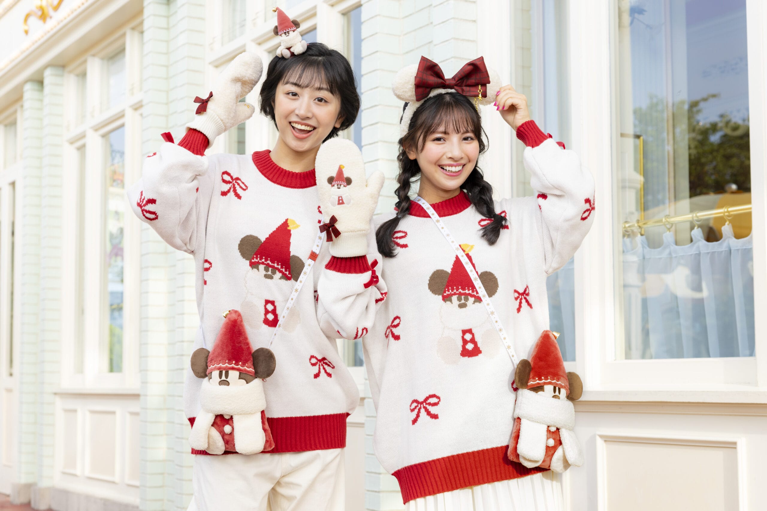Dos chicas de suéteres y accesorios festivos con una sonrisa con un ratón para Disneyland en Tokio Disneyland.