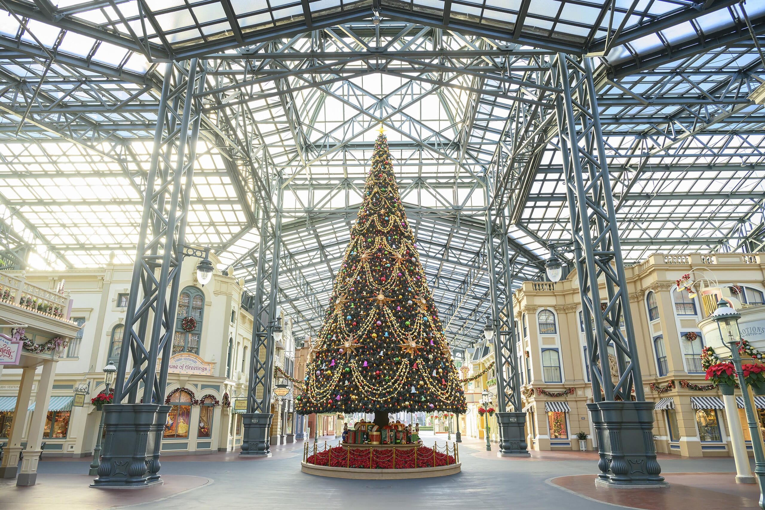 Un gran árbol de Navidad se encuentra en una plaza de techo de vidrio en Tokio Disneyland, con edificios festivos por todas partes.