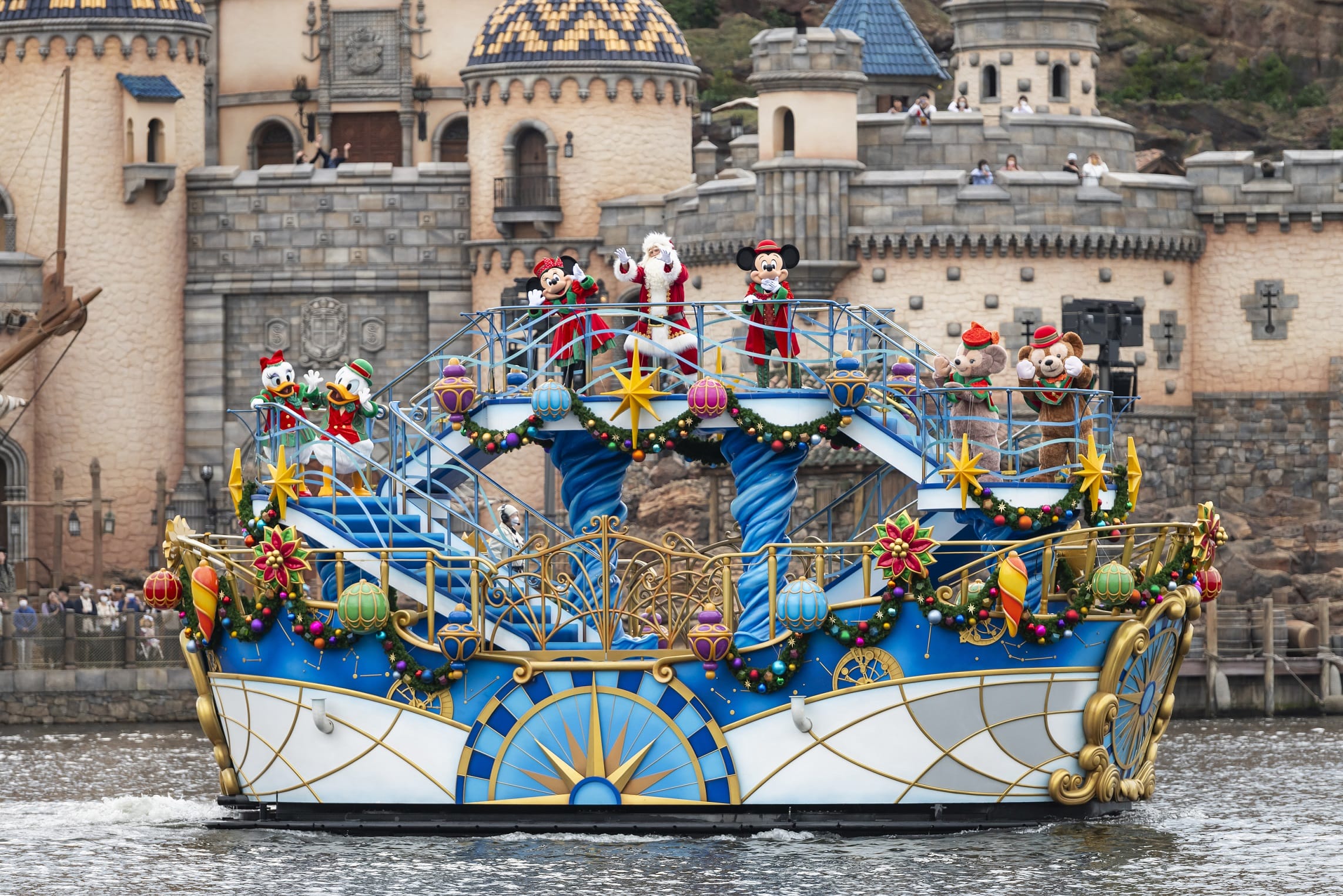 El colorido desfile de Navidad flota con los roles de Disney en el agua frente al fuerte en Tokio Disneyland.