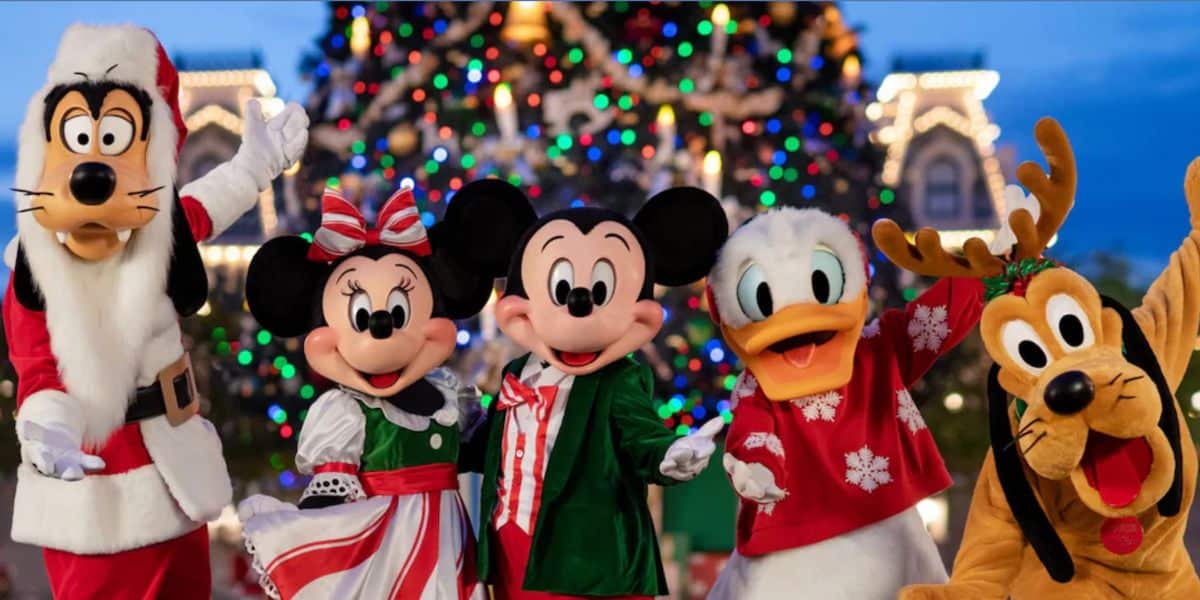 Goofy, Minnie Mouse, Mickey Mouse, el Pato Donald y Plutón vestidos con atuendos festivos se paran frente a un árbol de Navidad brillantemente iluminado, sonriendo y posando para una foto de felices fiestas en Magic Kingdom.