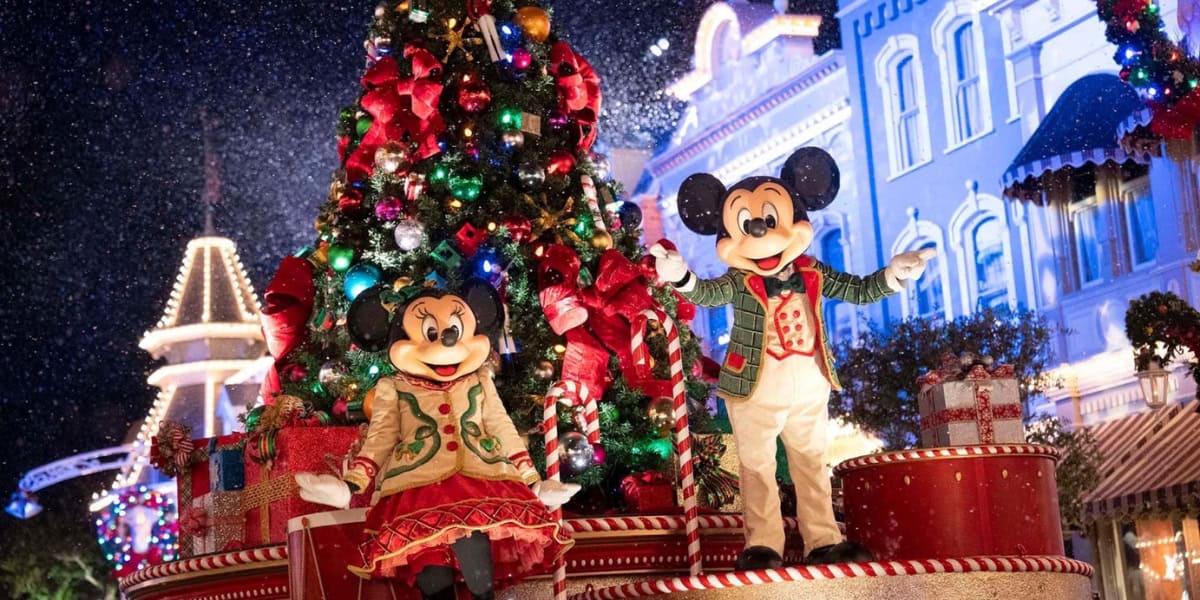 Mickey y Minnie Mouse, vestidos con atuendos festivos, se paran frente a un gran árbol de Navidad decorado en Disney World.