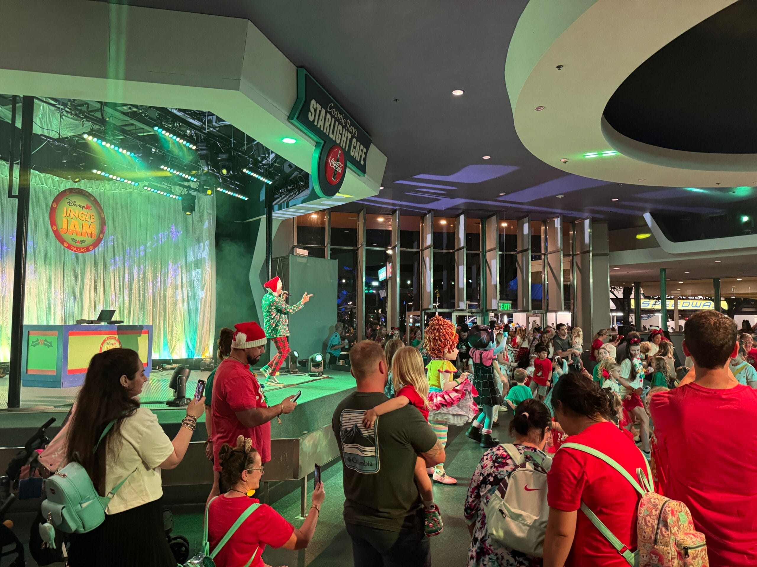 Una fiesta de Navidad muy feliz es un evento festivo en el interior con un actor en el escenario entreteniendo a la multitud. Personas vestidas con colores brillantes y atuendos festivos capturan los recuerdos con sus cámaras.
