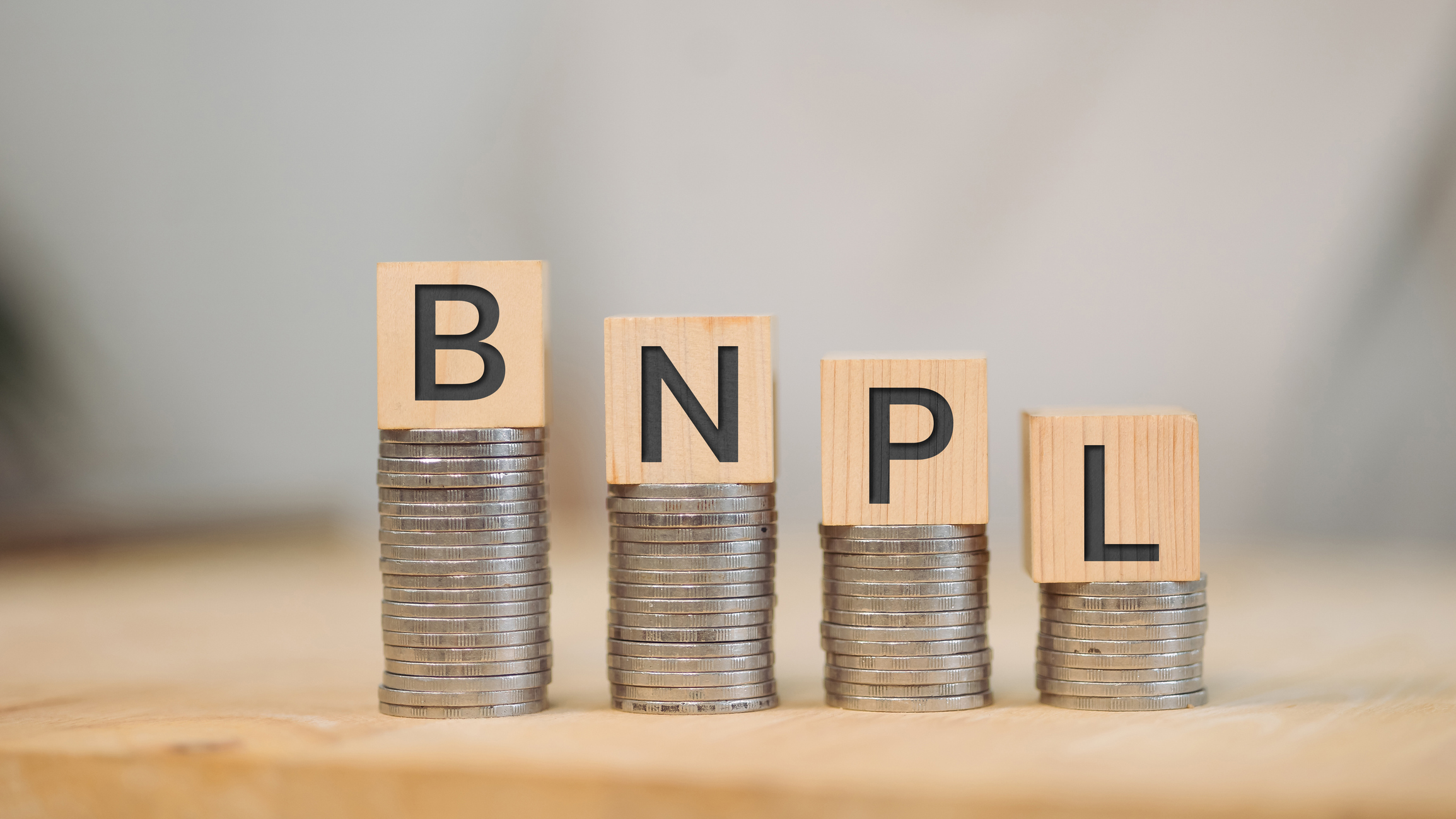 Primer plano de bloques de madera que deletrean BNPL colocados sobre pilas de monedas.
