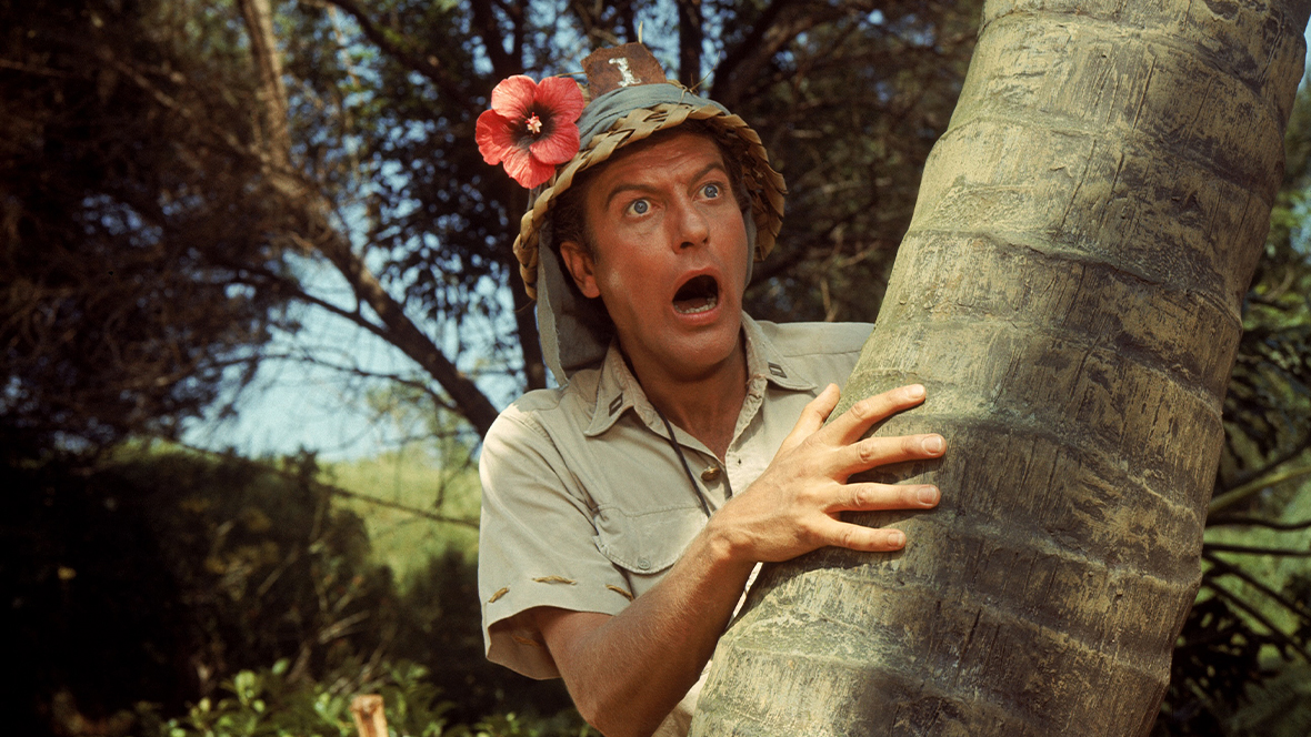 Una fotografía de 1966 del teniente Robin Crusoe del USN Van Dyke muestra a la leyenda de Disney Dick Van Dyke con un bombín con flores y haciendo una mueca, vista fuera de cámara.