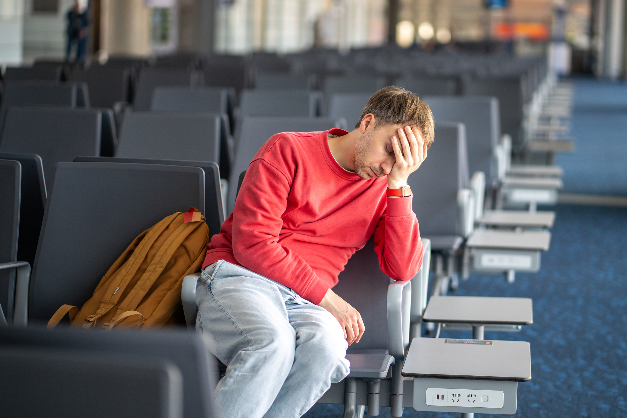 Un hombre cansado y dormido se desploma contra una silla en la zona de espera de un aeropuerto. Largas escalas, cansancio por la espera, vuelos retrasados, sueño profundo, desánimo por el tiempo interminable en el aeropuerto.