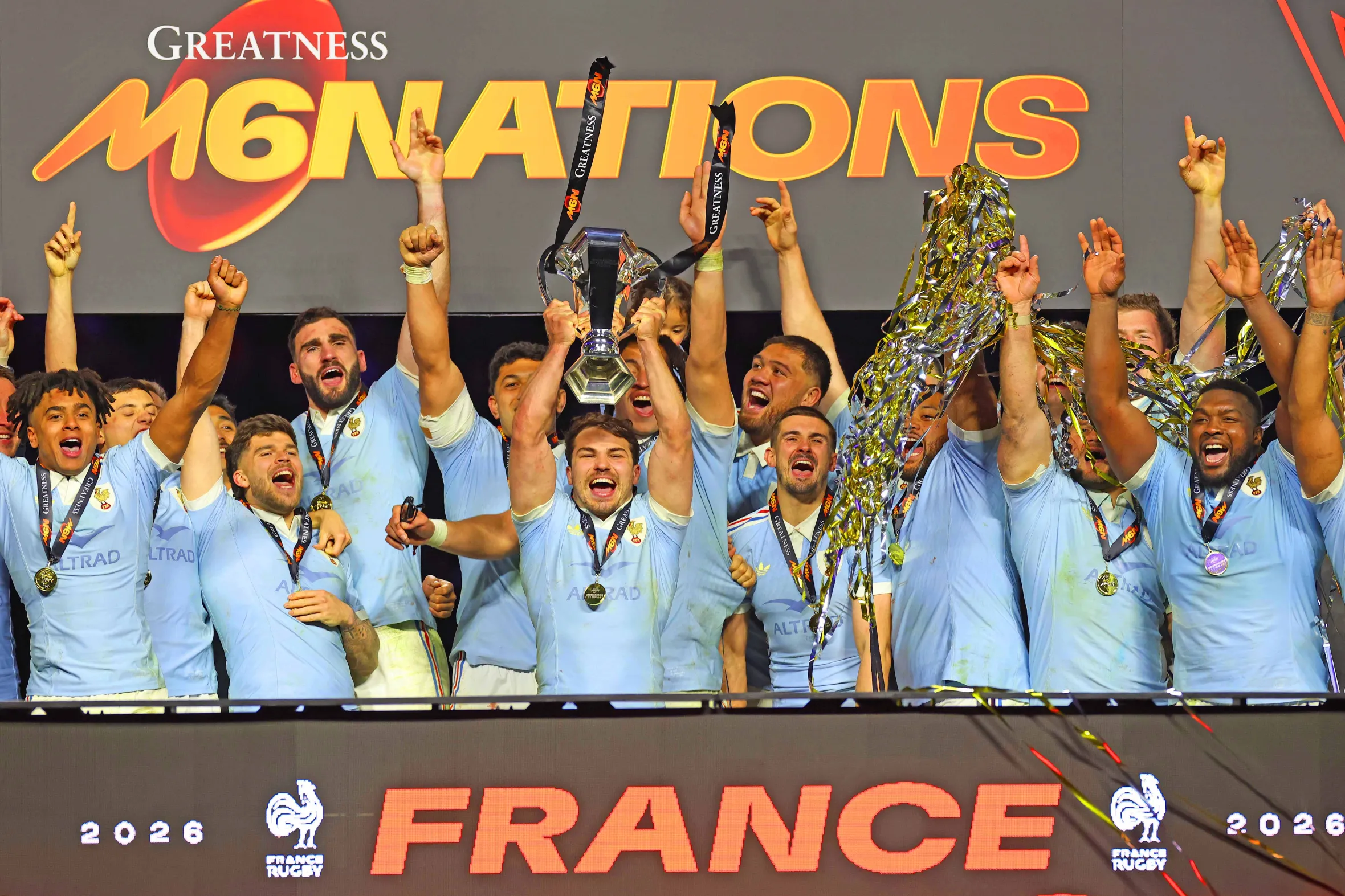 Jugadores de rugby celebrando con trofeos y medallas en un escenario. 