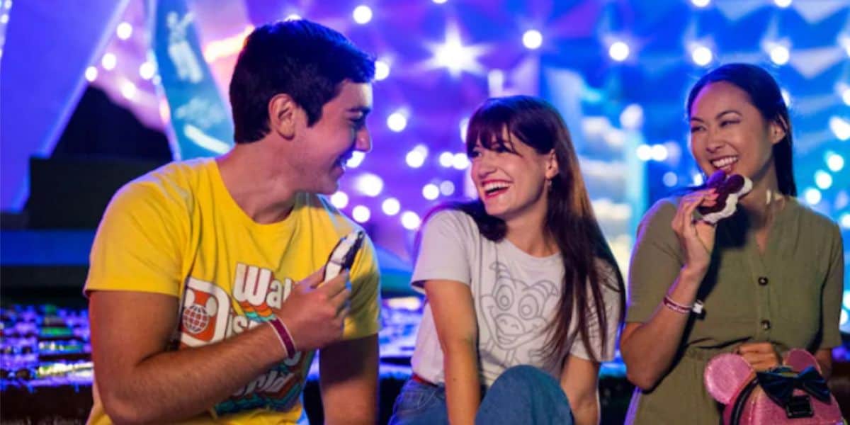 Tres visitantes de Disney World disfrutan de un helado frente a la nave espacial Earth de EPCOT por la noche.