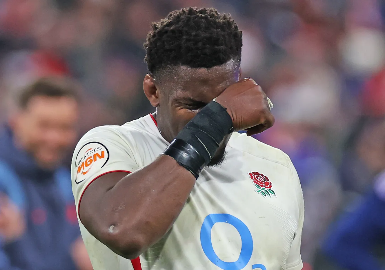 Un jugador de rugby con una camiseta blanca con la insignia de una rosa roja y la mano tapándose los ojos como si sufriera dolor.