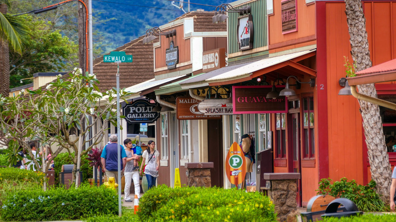 Los turistas caminan por una hilera de coloridas tiendas con carteles.