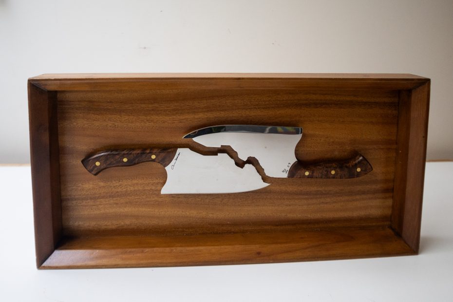 Una caja de madera parte un cuchillo grande por la mitad, con las dos mitades alineadas en el centro de la caja.