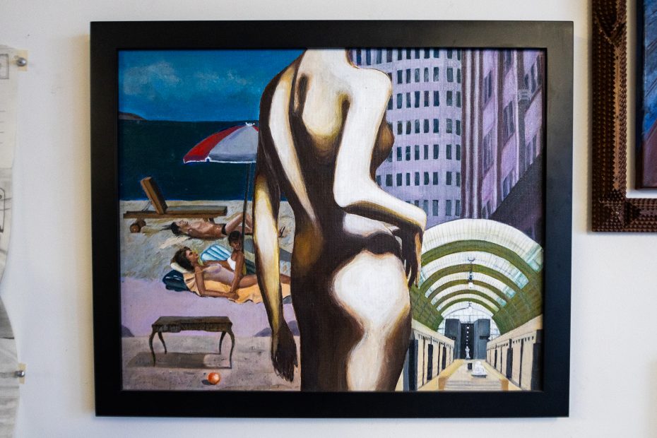 Una pintura enmarcada de una figura desnuda en primer plano con una escena de playa y edificios al fondo, mezclando estilos realistas y realistas.