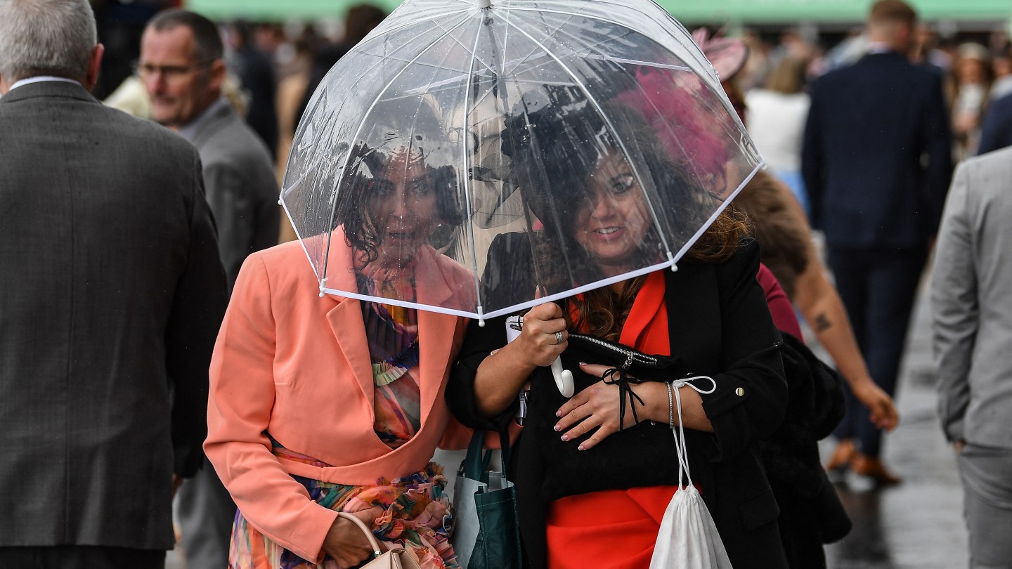 Los asistentes a las carreras intentan evitar la lluvia en el último día de la carrera de caballos del Gran Festival Nacional.