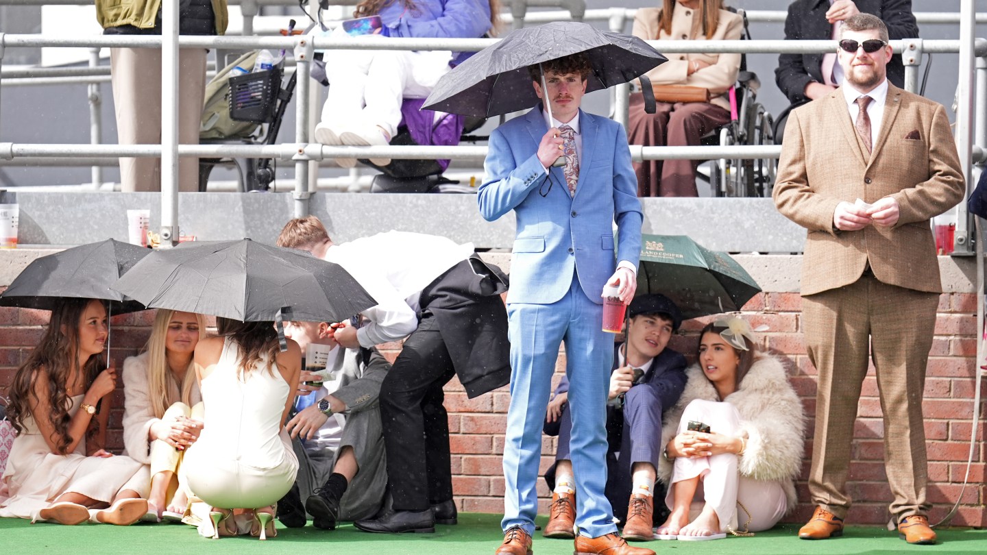 Los corredores se protegen de la lluvia en el Gran Día Nacional del Gran Festival Nacional Randex 2026 en el hipódromo de Aintree.