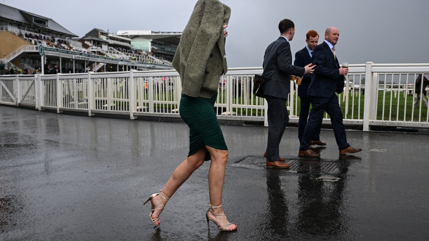 Un aficionado a las carreras (C) se protege de la lluvia el último día de la carrera de caballos del Gran Festival Nacional en el hipódromo de Aintree.