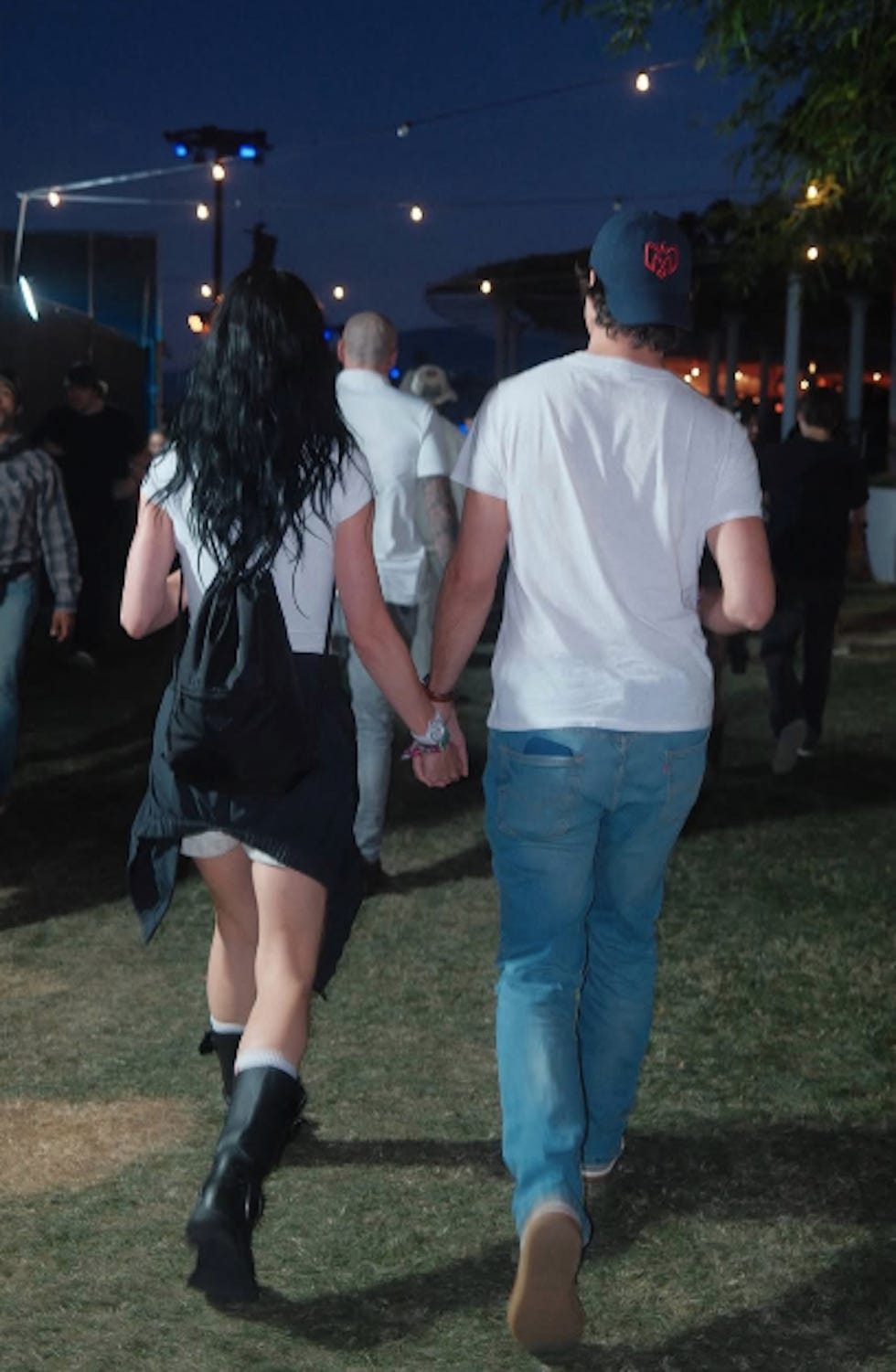 Pareja caminando de la mano en un evento al aire libre al atardecer.