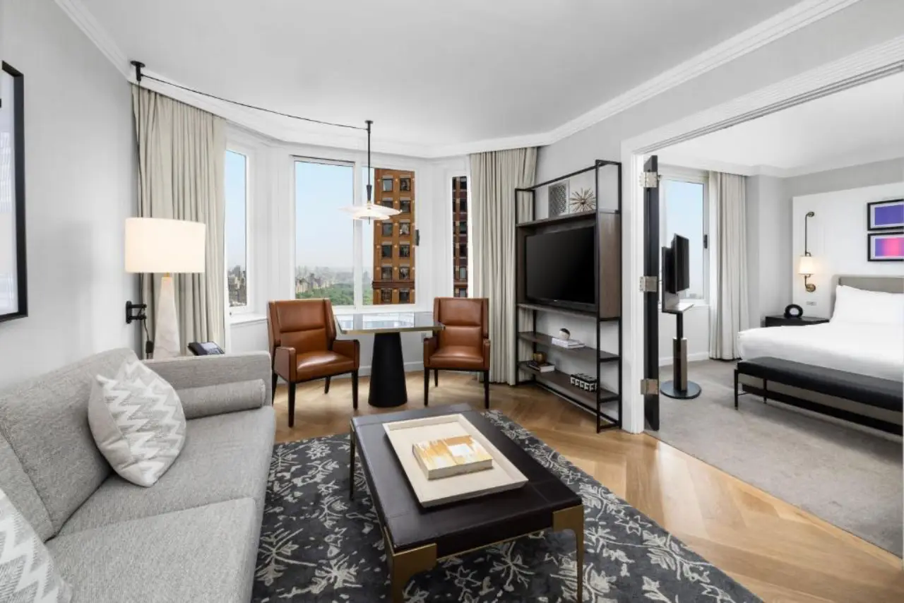 Londres Nueva York regresa a Midtown bajo el Marriott Luxury Collection 3 Una espaciosa suite king de un dormitorio en Londres, un hotel Luxury Collection en Nueva York, con una sala de estar independiente, pisos de madera en forma de espiga y ventanales con vistas a Central Park.